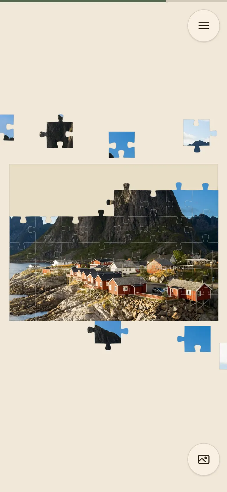 a puzzle part way through: a photograph of red cabins below a Norwegian mountain, partly assembled on the board, with loose pieces lying around it