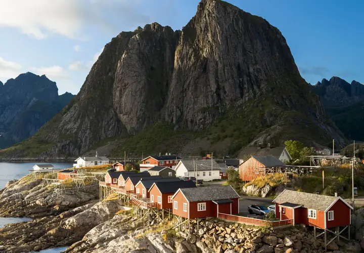 a printed photograph of red cabins on a rocky shore below a steep Norwegian mountain